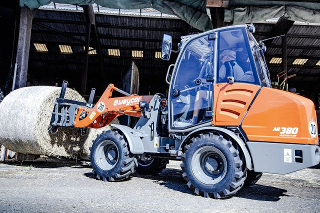 Radlader Weycor AR 380 hebt Rundballen auf landwirtschaftlichem Hof.