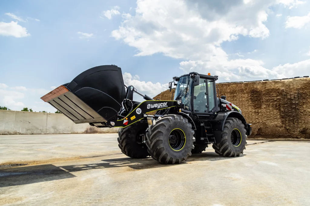 Weycor Radlader AR 680 Black Edition mit großer Schaufel auf Betonfläche, im Hintergrund ein Silagehaufen unter wolkigem Himmel.