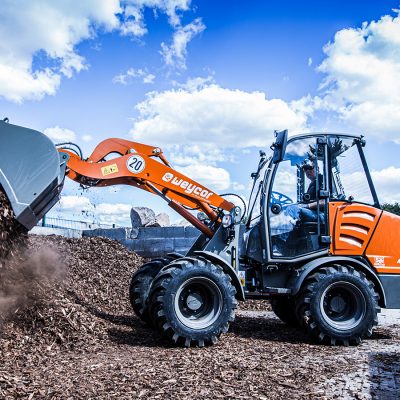 Weycor Radlader AR 380 beim Entladen von Hackschnitzeln, Seitenansicht unter blauem Himmel mit leichten Wolken.