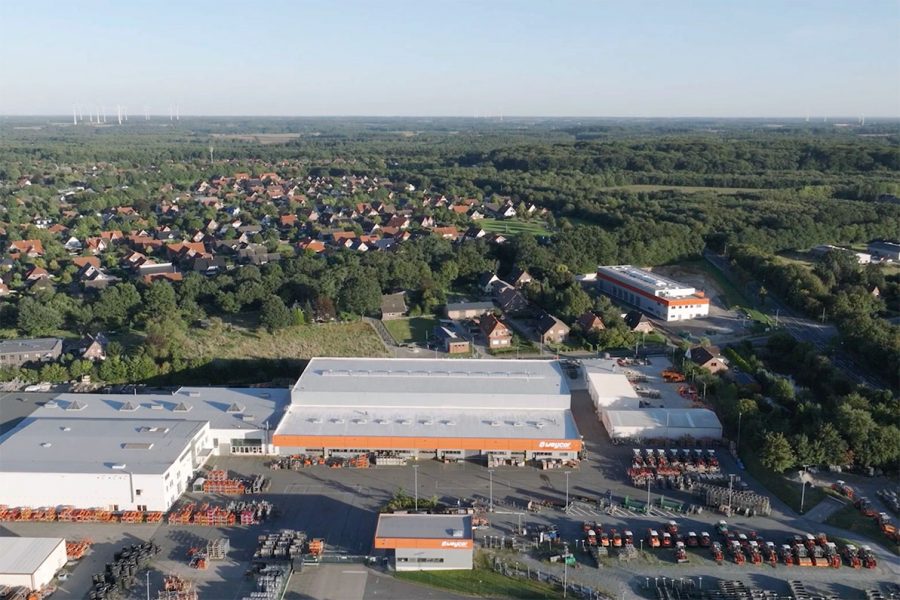 Luftaufnahme des Weycor-Werksgeländes mit Produktionshallen, Lagerflächen und Maschinenpark, im Hintergrund Wohnsiedlung und bewaldete Landschaft.