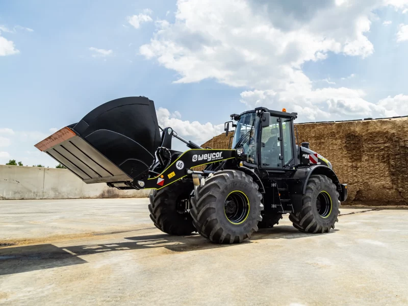 Weycor Radlader AR 680 Black Edition mit großer Schaufel auf Betonfläche, im Hintergrund ein Silagehaufen unter wolkigem Himmel.