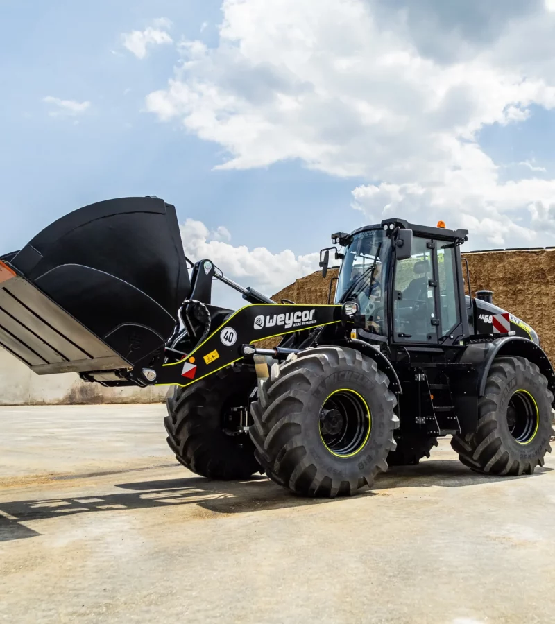 Weycor Radlader AR 680 Black Edition mit großer Schaufel auf Betonfläche, im Hintergrund ein Silagehaufen unter wolkigem Himmel.