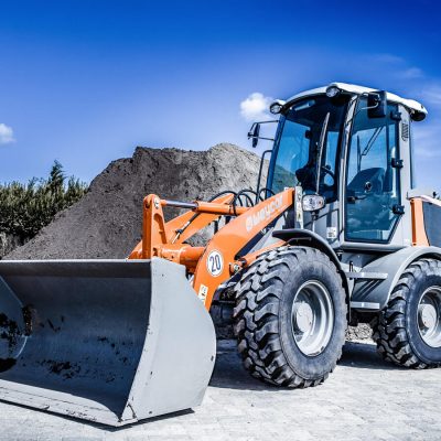 Weycor Radlader AR 440 frontal schräg fotografiert, steht vor einem großen Erd- und Sandhaufen, blauer Himmel mit wenigen Wolken im Hintergrund.