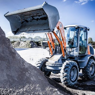 Weycor Radlader AR 480T mit hochgehobener Schaufel beim Aufnehmen von Erdmaterial an einem Lagerplatz unter freiem Himmel.