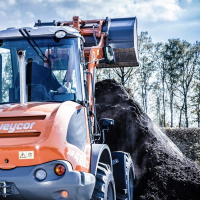 Weycor Radlader AR 480S frontal im Einsatz beim Aufnehmen von Erde, im Hintergrund Bäume und blauer Himmel.