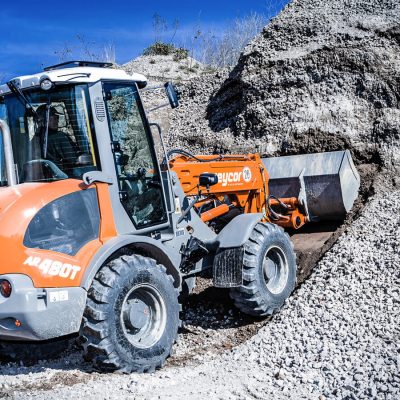 Weycor AR 480 T Radlader mit Ladeschaufel bei der Aufnahme von Schottermaterial an einem steilen Abhang.