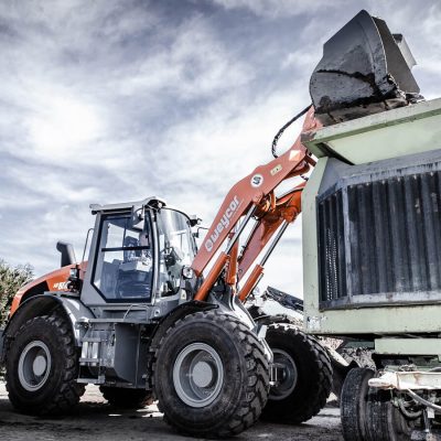 Weycor AR 660 Radlader mit hoch angehobener Schaufel vor Erdhügeln.